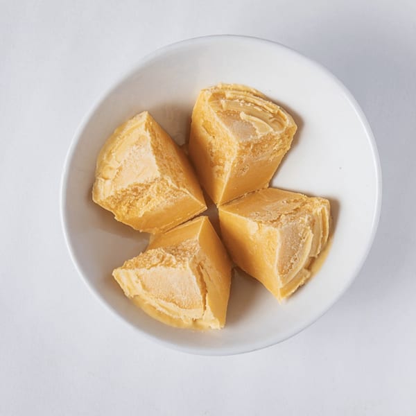 Four pieces of yellow, flaky Khuwa, a traditional Nepalese dairy product, in a white bowl.
