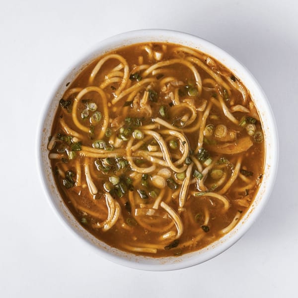 A close-up, overhead view of a bowl of Nepalese thukpa noodle soup with broth and green onions.