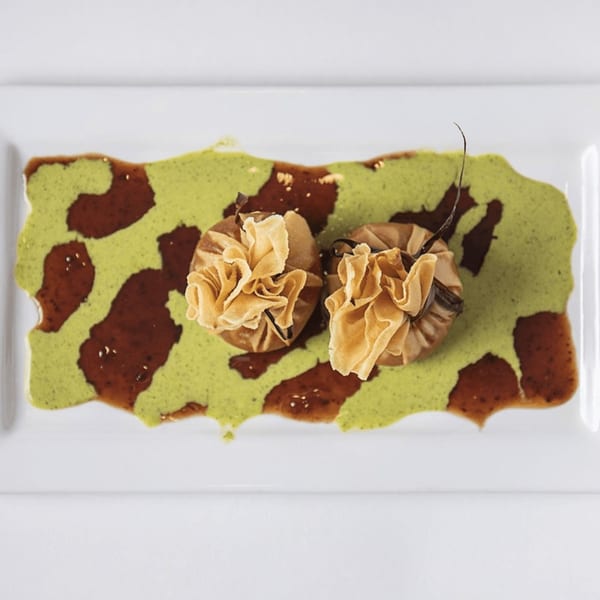 Two Nepalese dumplings with ruffled tops, on a white plate with green and brown sauces.