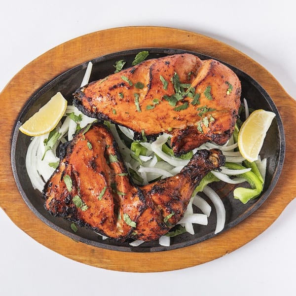 Tandoori chicken, garnished with cilantro, onions, bell peppers, and lemon wedges on a sizzling platter.