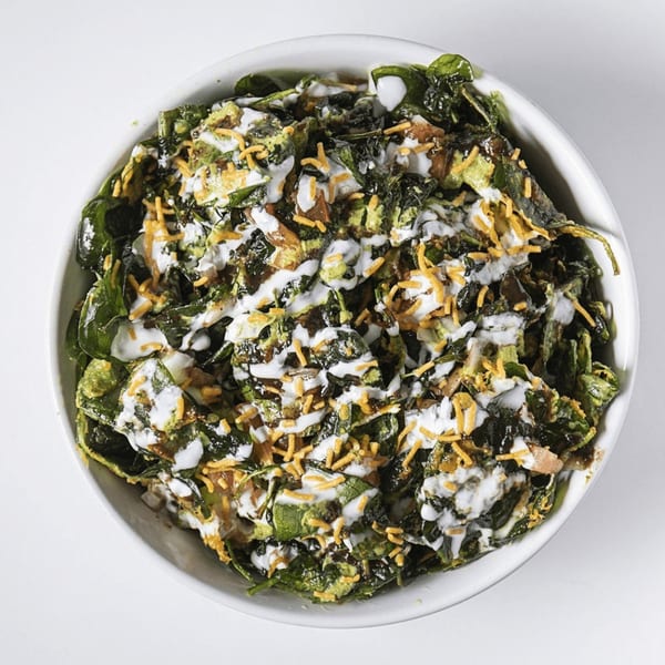 A white bowl filled with green leafy salad, drizzled with white sauce and topped with orange crispy bits.
