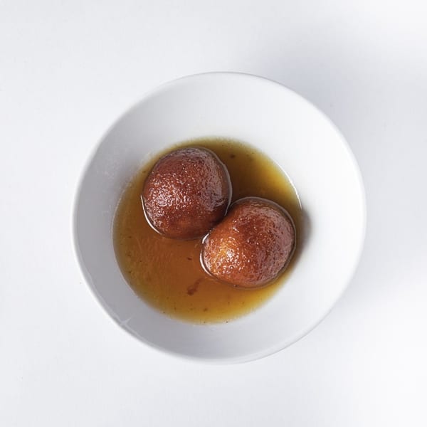 Two gulab jamun, a Nepalese dessert, soaked in syrup in a white bowl.