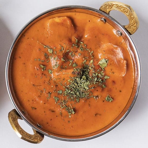 Close-up of a Nepalese curry in a metal bowl with ornate brass handles, garnished with dried herbs.