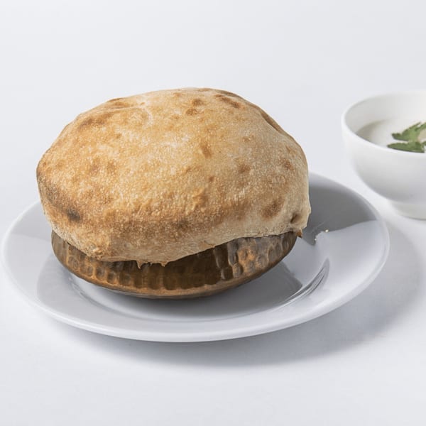 A golden-brown bread dome covers a bowl on a white plate, with a small white sauce bowl beside it.