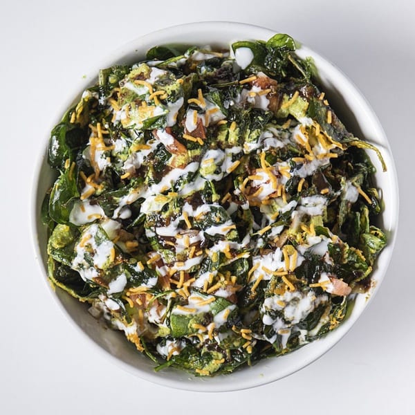 Overhead view of a bowl of crispy spinach chaat with yogurt, chutneys, and crunchy toppings.