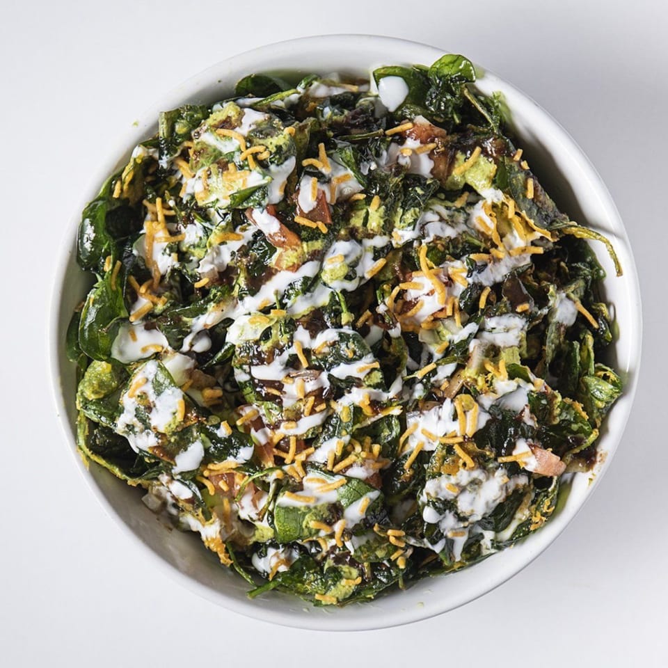 Overhead view of a bowl of crispy spinach chaat with yogurt, chutneys, and crunchy toppings.