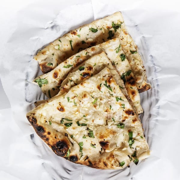 Four pieces of garlic naan bread, garnished with cilantro, served in white parchment paper.