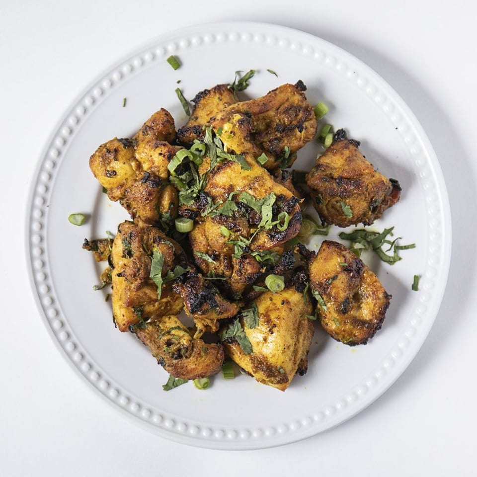 Grilled chicken pieces, seasoned and garnished with fresh herbs, served on a white plate.