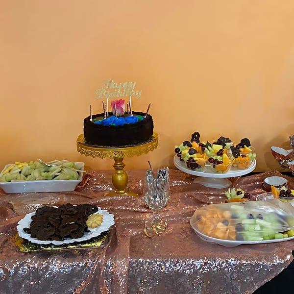 A birthday cake, fruit cups, and cookies on a sequined table at Yak and Yeti Himalayan Cuisine.