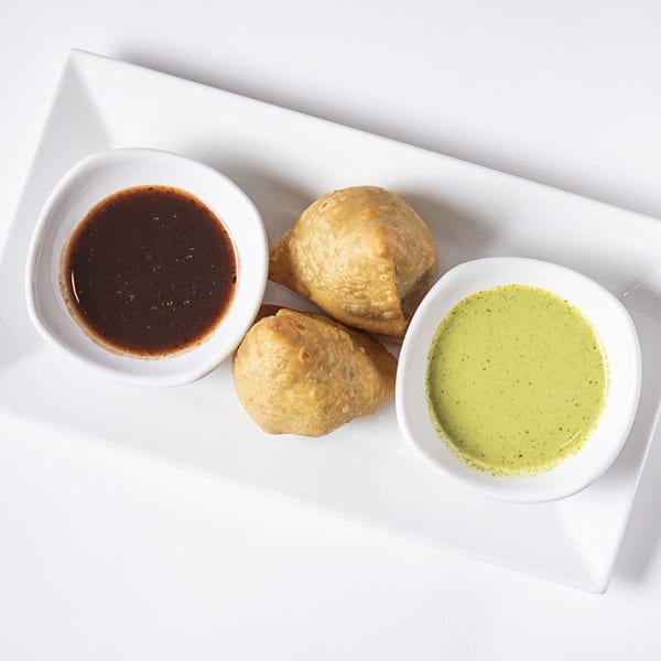 Two golden-brown Nepalese samosas with dark and light green dipping sauces on a white rectangular plate.
