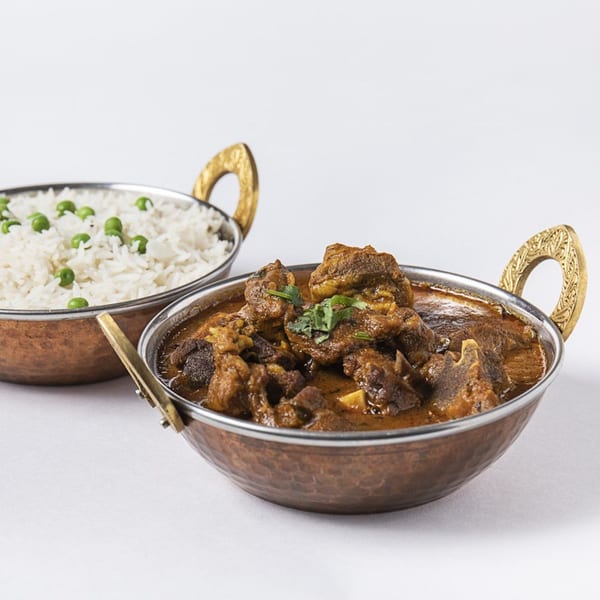 Two copper bowls, one with Nepalese lamb curry, the other with white rice and green peas.