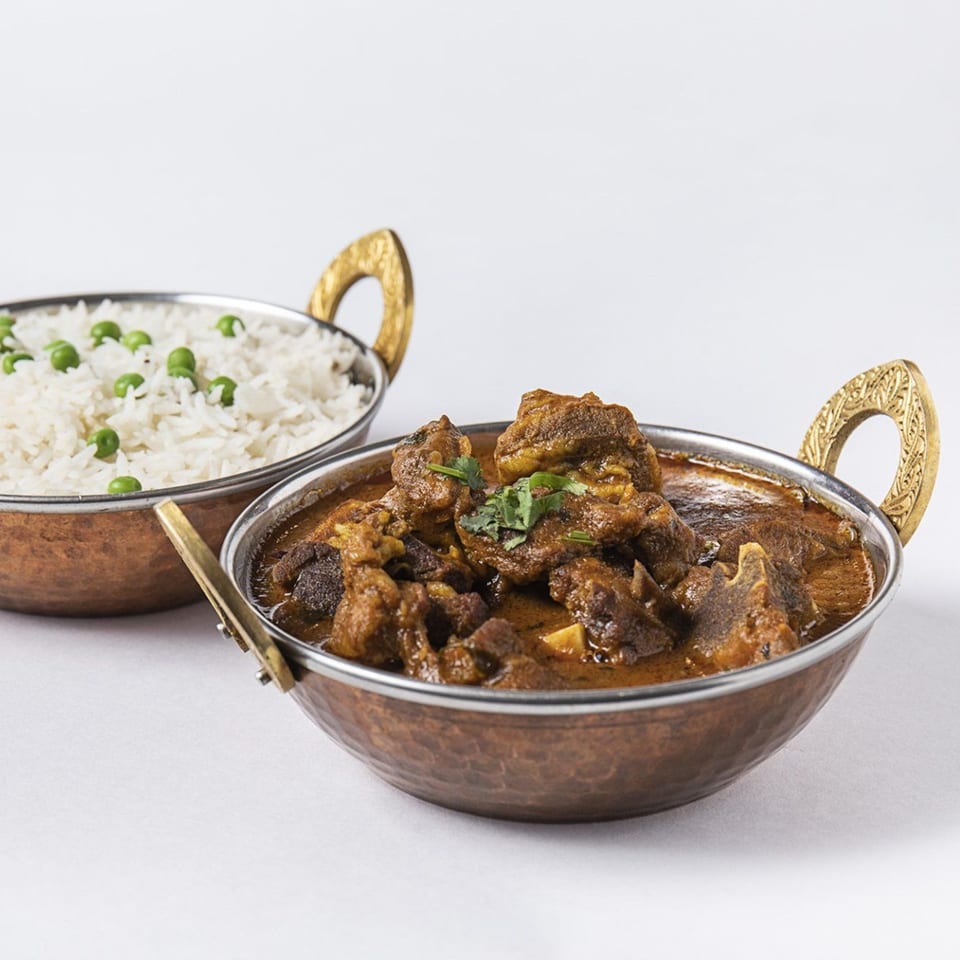Two copper bowls, one with Nepalese lamb curry, the other with white rice and green peas.
