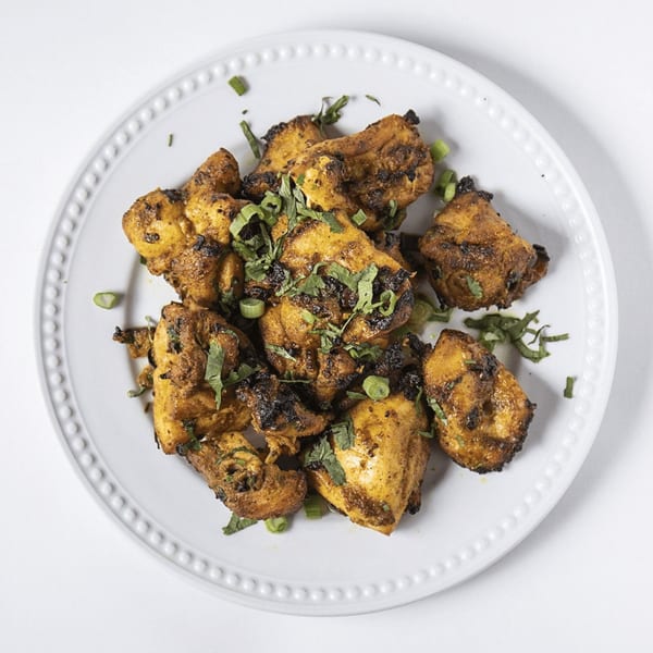 Grilled chicken pieces, seasoned and garnished with fresh herbs, on a white plate.